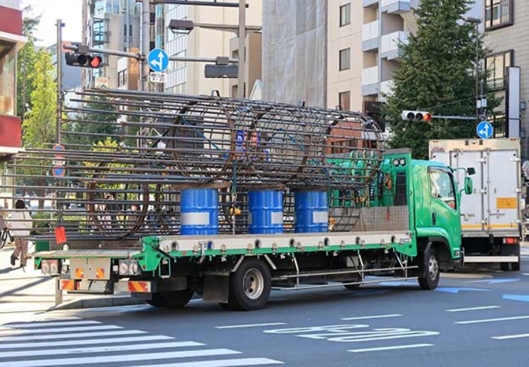 大きい杭や鉄筋鉄骨の部材を載せたトラックが走っている写真